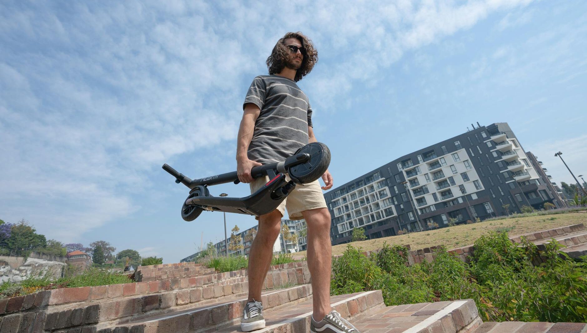 man in grey t shirt and shorts holding folded electric scooter