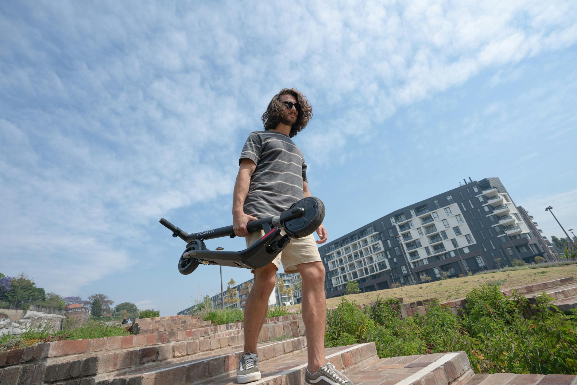 man in grey t shirt and shorts holding folded electric scooter